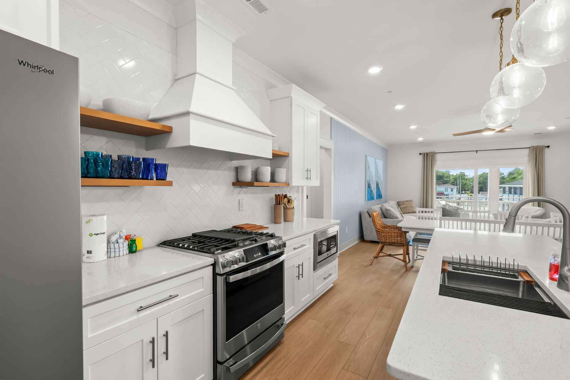 Bright modern white kitchen with stainless appliances, island sink, and dining area beyond.