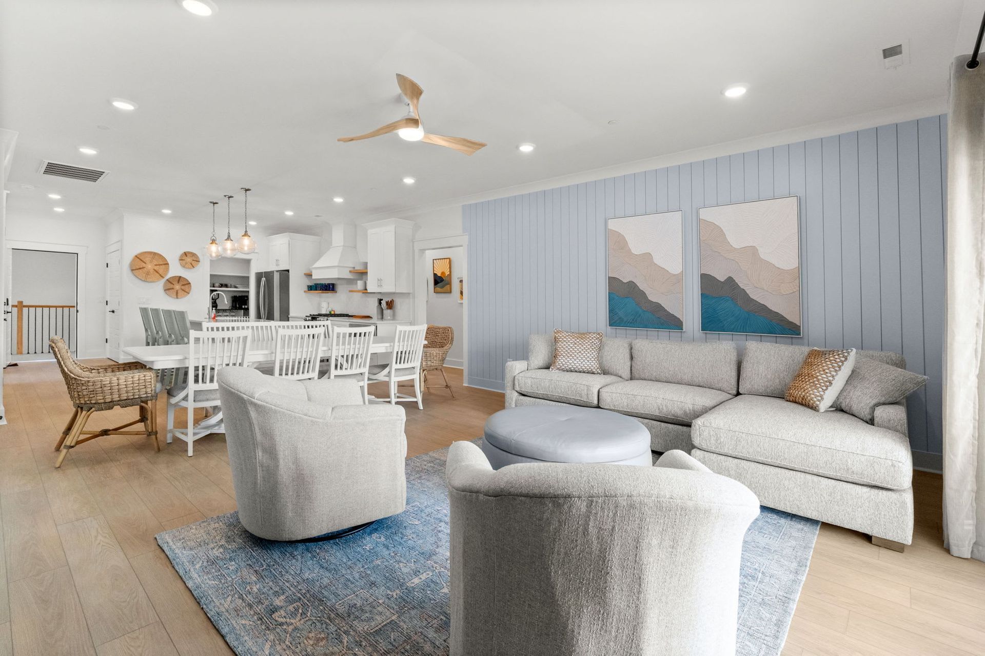 Bright open-plan living room with white sofas, blue rug, dining area, and kitchen in the background