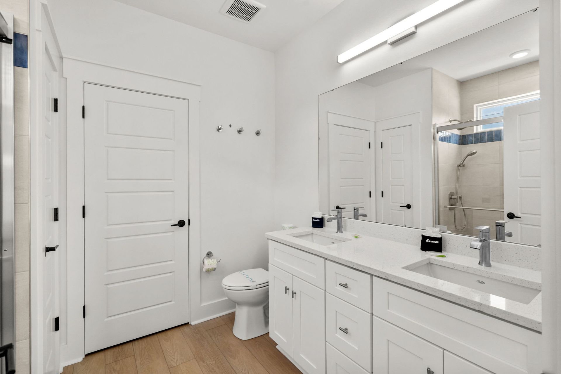 Bright white bathroom with double vanity, large mirror, toilet, and shower.