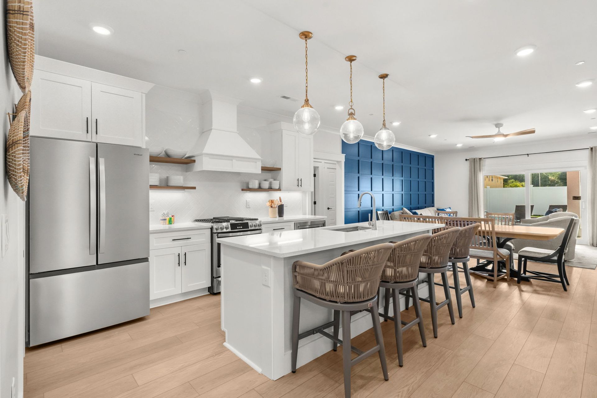 Bright modern kitchen and dining area with white cabinets, island seating, stainless steel fridge, and blue accent wall