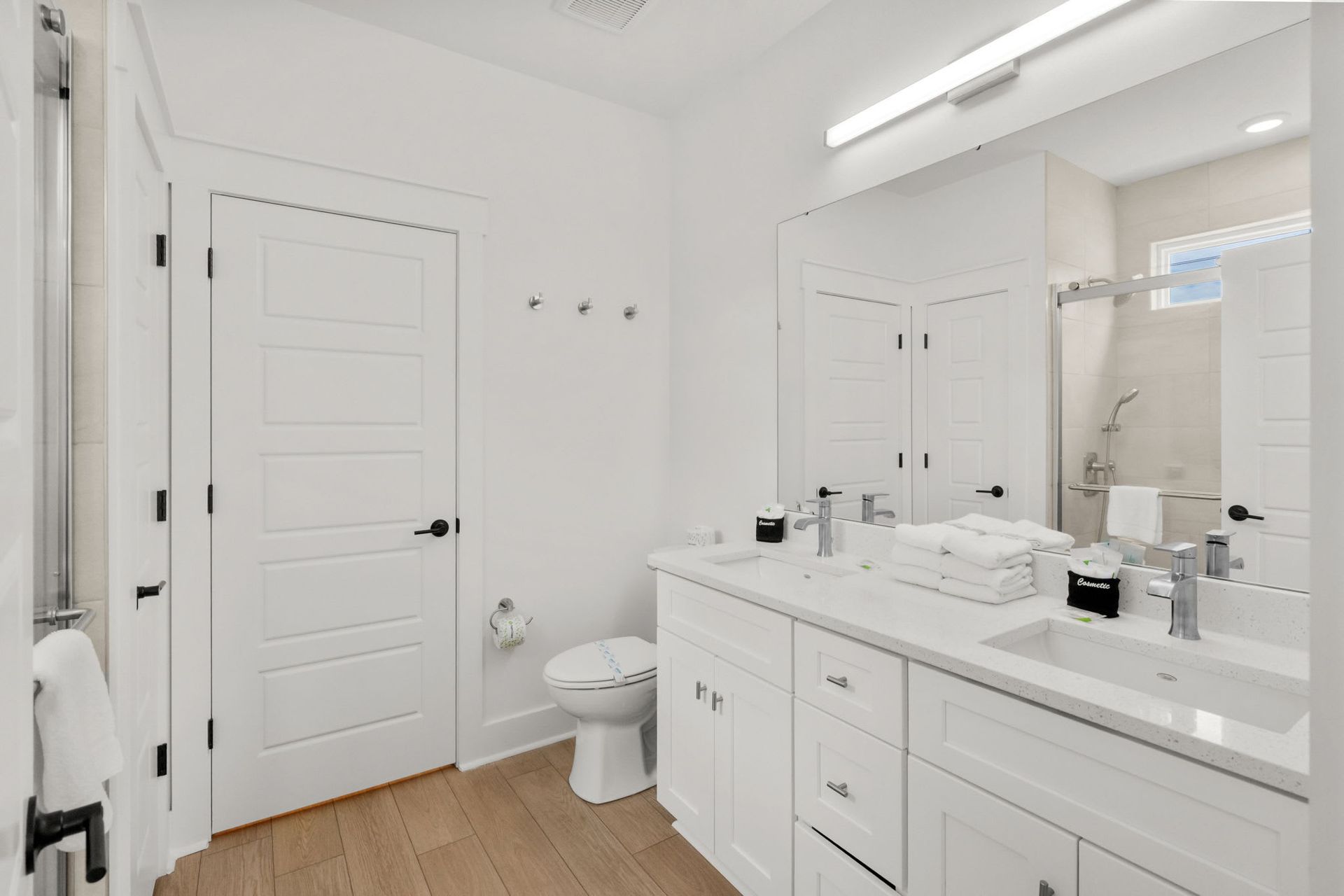 Bright white bathroom with vanity, mirror, toilet, and light wood floor