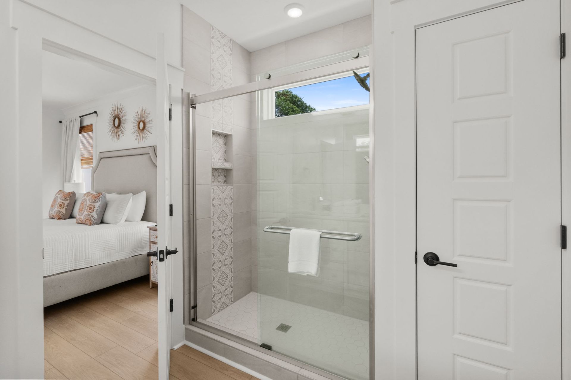 Bright white bedroom with en suite glass shower and open door, modern clean bathroom view