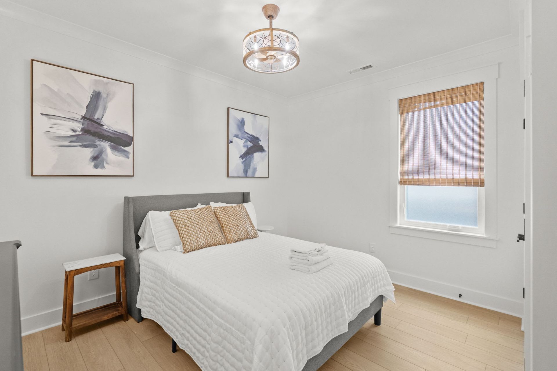Bright bedroom with white walls, a bed, framed bird art, and a window with a striped blind.