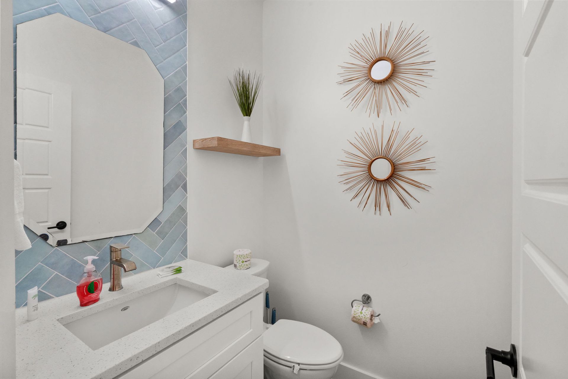 Bright white bathroom with a vanity, round mirror, and decorative wall sunbursts.