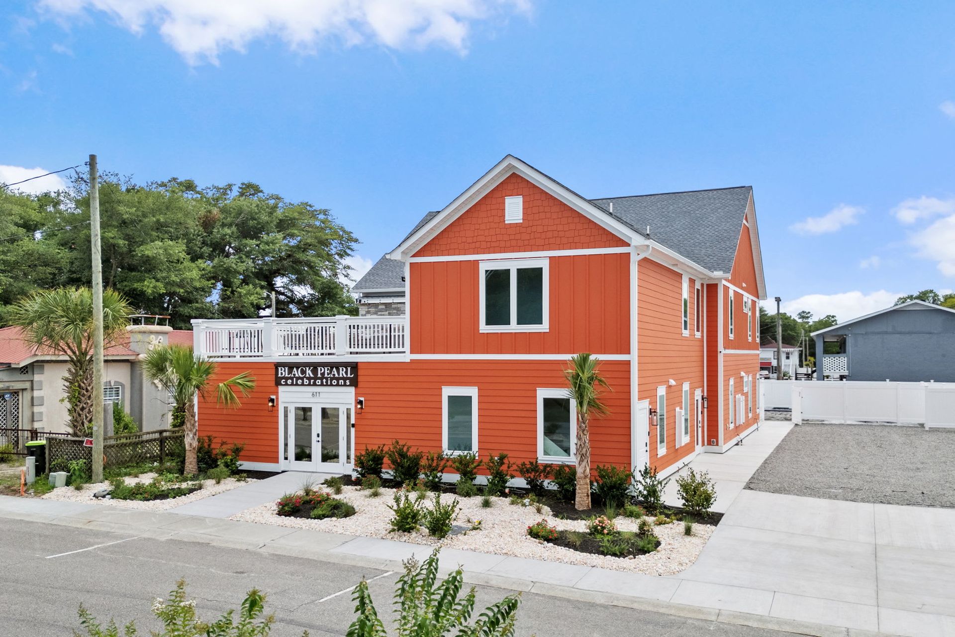 Bright orange two-story house with white trim, front porch, and gray driveway on a sunny street