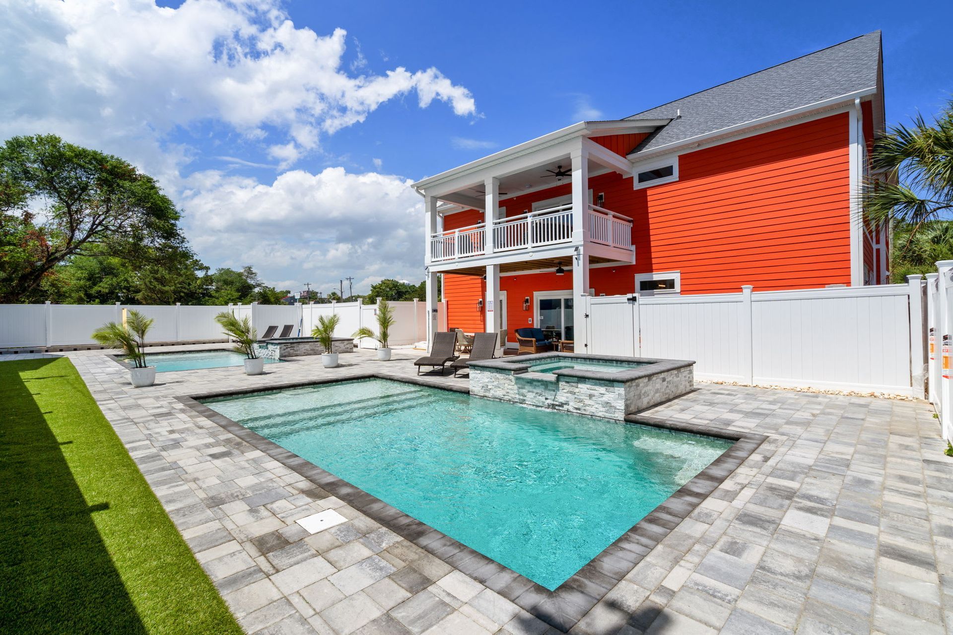 Backyard with turquoise pool, stone patio, and modern orange house under a blue sky