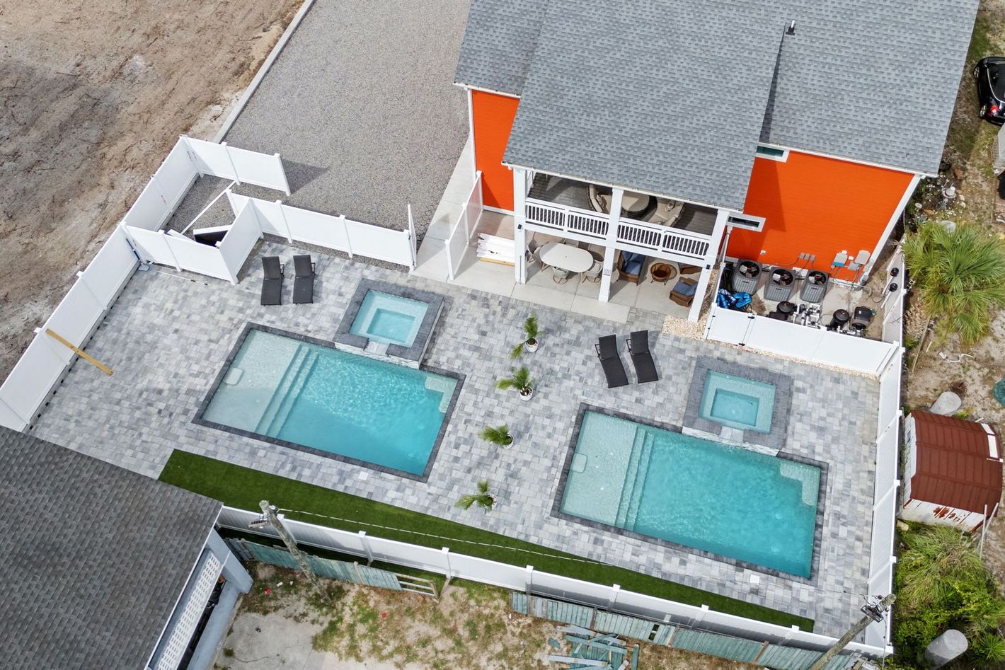 Aerial view of a house with two rectangular swimming pools and lounge chairs on a patio