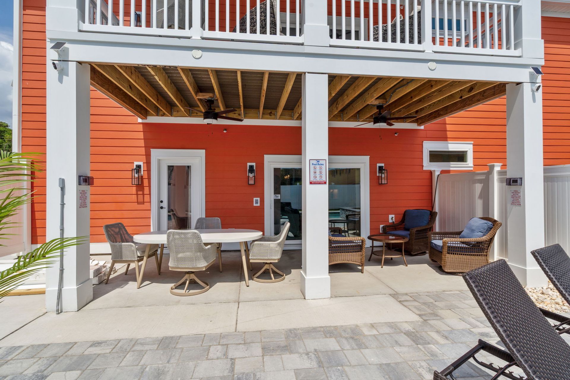 Outdoor patio beneath a deck with wicker chairs, table, and an orange exterior wall