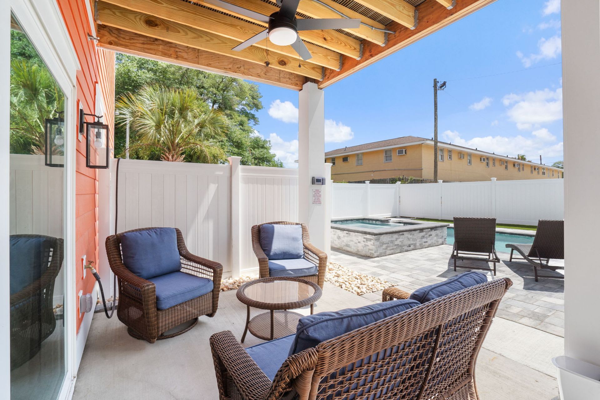 Covered patio with wicker chairs, a table, and a fenced outdoor seating area in bright sunlight