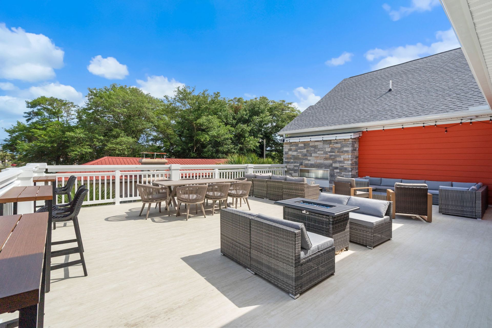 Rooftop patio with wicker seating, tables, and blue sky view beside a red building