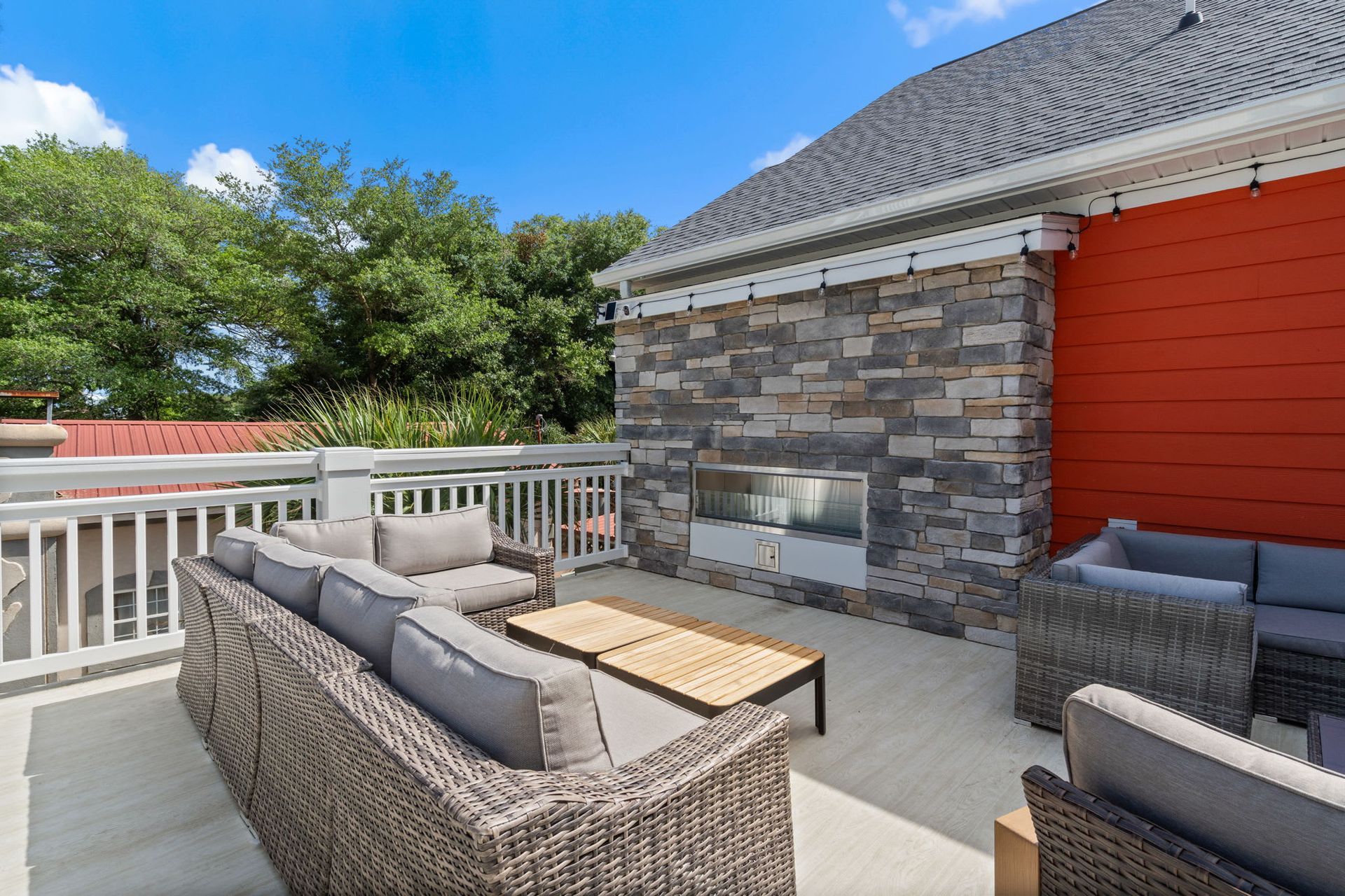 Patio with wicker seating, gray cushions, stone wall, and red siding beside a white railing
