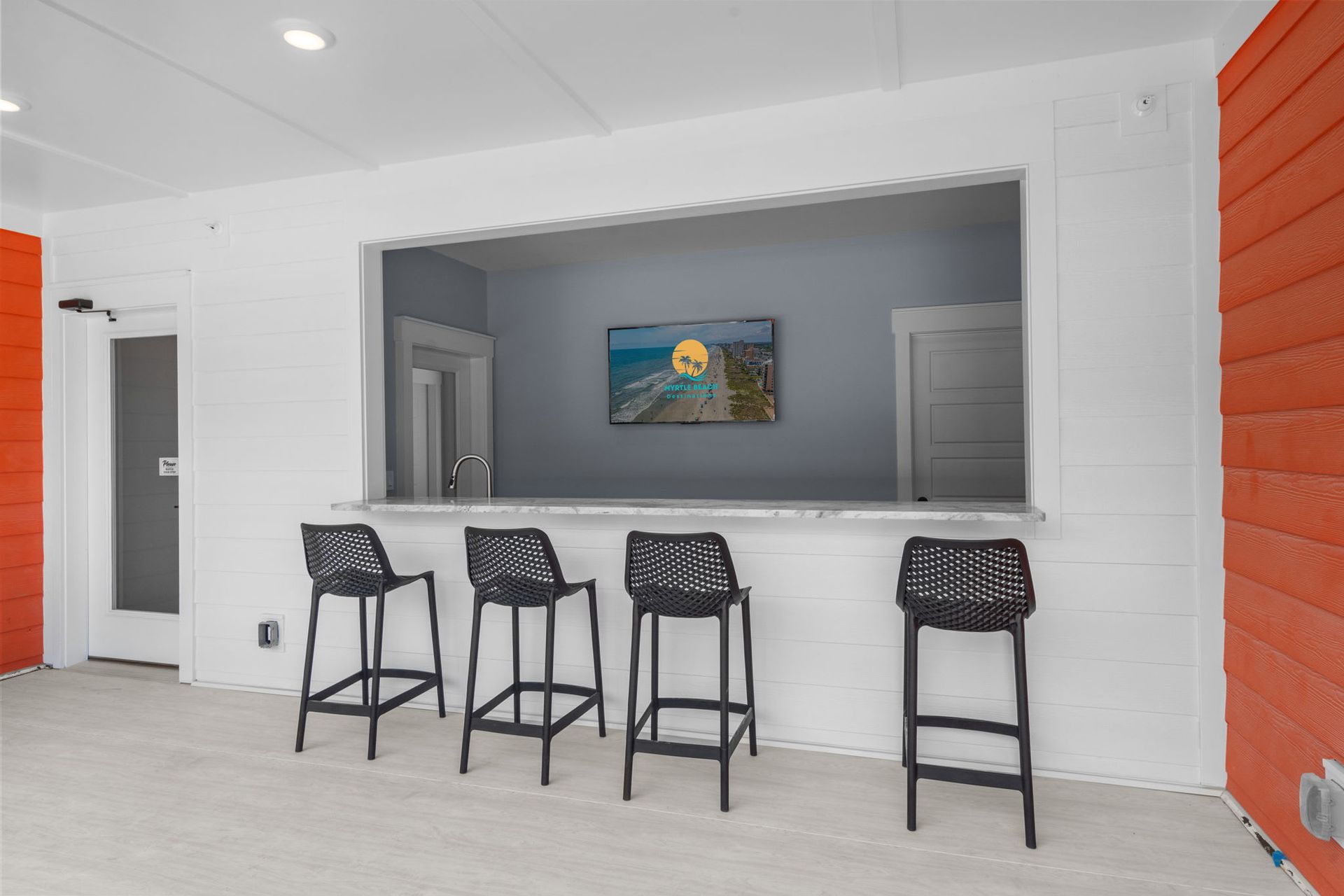 Covered patio with four black bar stools facing a serving window and orange accent walls