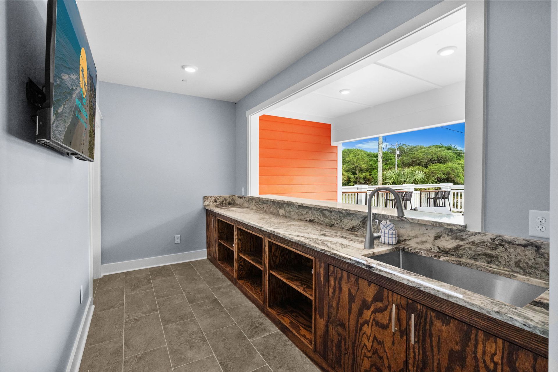 Modern kitchen with long granite island, wood cabinets, and large pass-through window to outdoor view