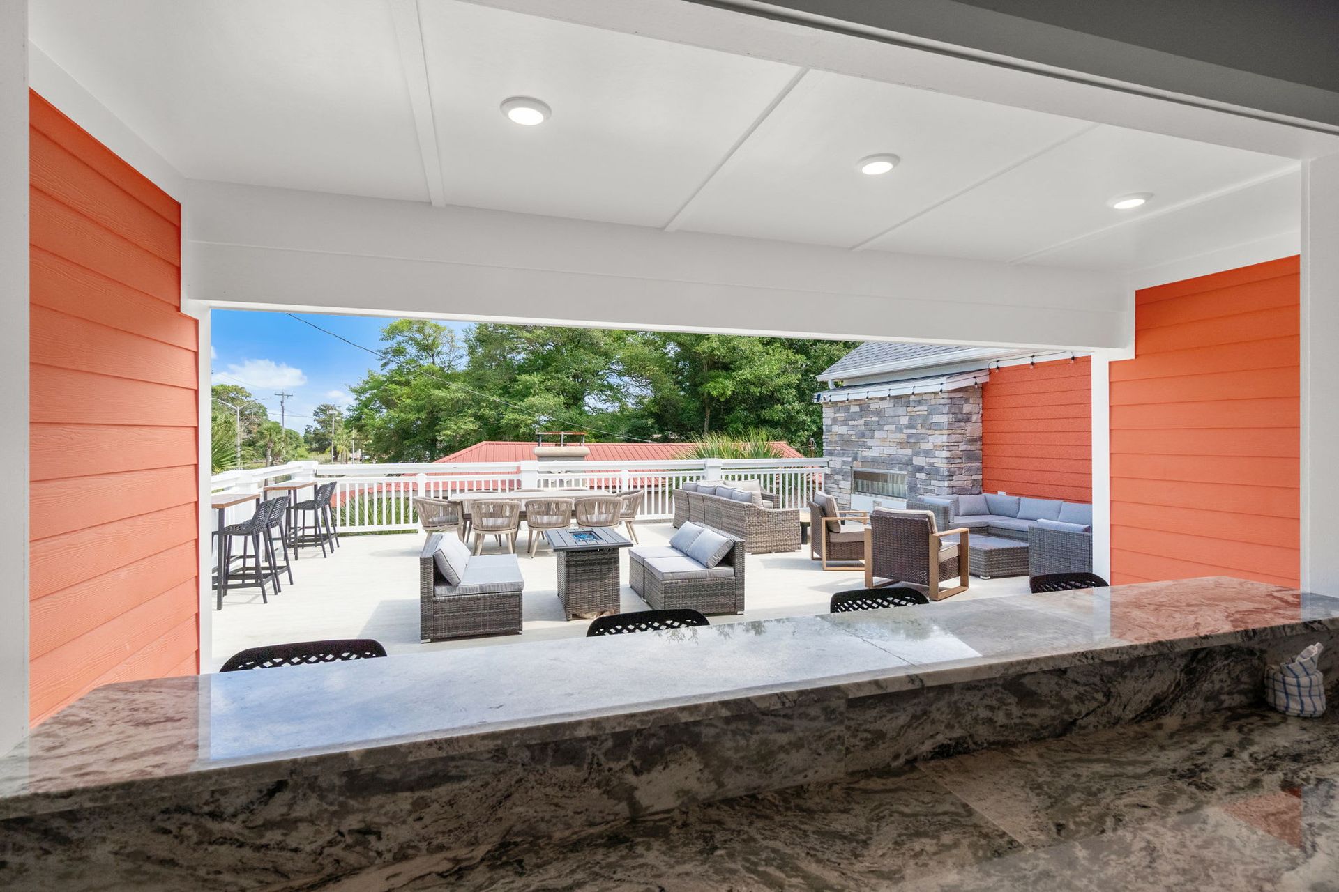 Covered patio with stone bar, wicker seating, and an outdoor pool area beyond, framed by orange walls