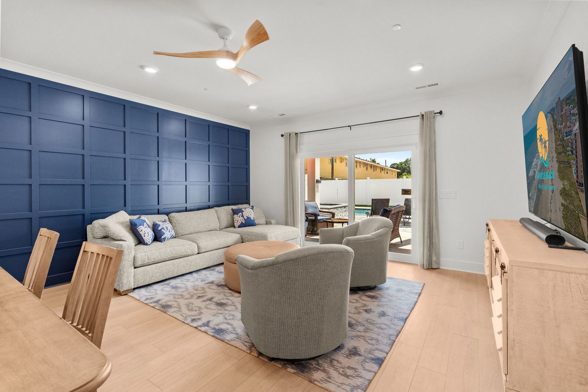 Bright living room with blue accent wall, beige sofa, gray chairs, and sliding doors to a patio.