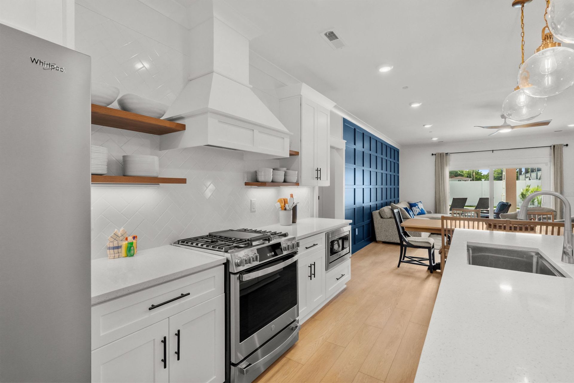 Bright modern kitchen with white cabinets, wood floors, and a dining area beside large windows
