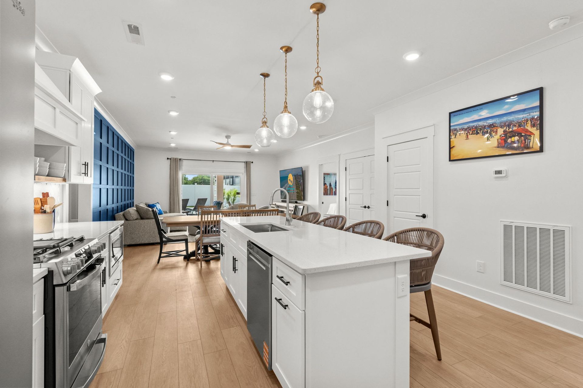 Bright open kitchen with white island, wood floors, pendant lights, and blue built-in cabinets.