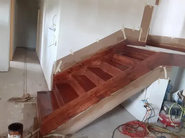 A wooden staircase is being painted in a room.