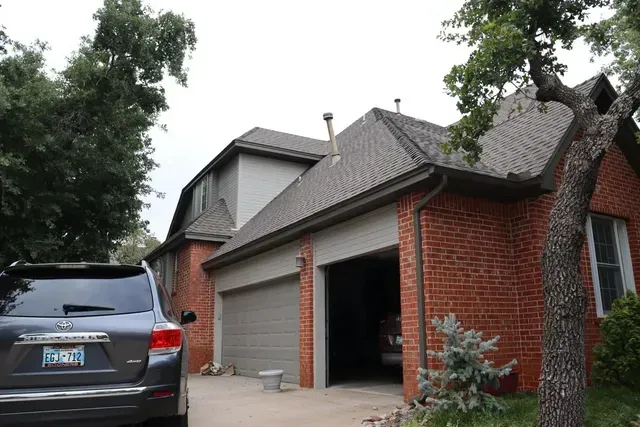 A car is parked in front of a brick house with a garage.