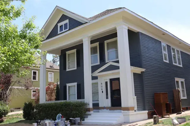 A large house with a blue siding and white trim is being painted.