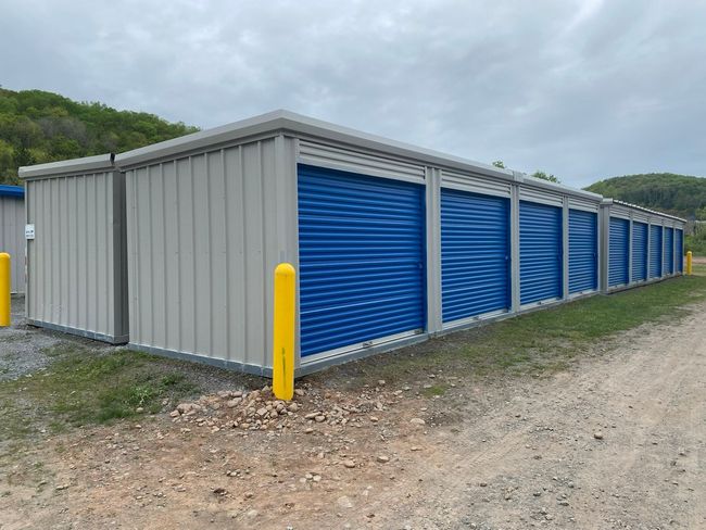 Gray storage buildings with blue doors and yellow bollards at the corners of each building.