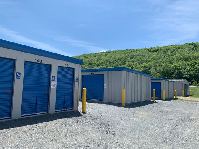 Four gray storage buildings with blue doors and yellow bollards at the corners of each building.