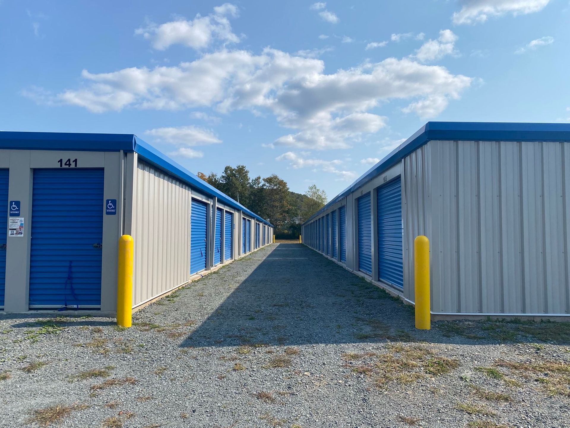 Two gray storage buildings with blue doors and yellow bollards at the corner of each building