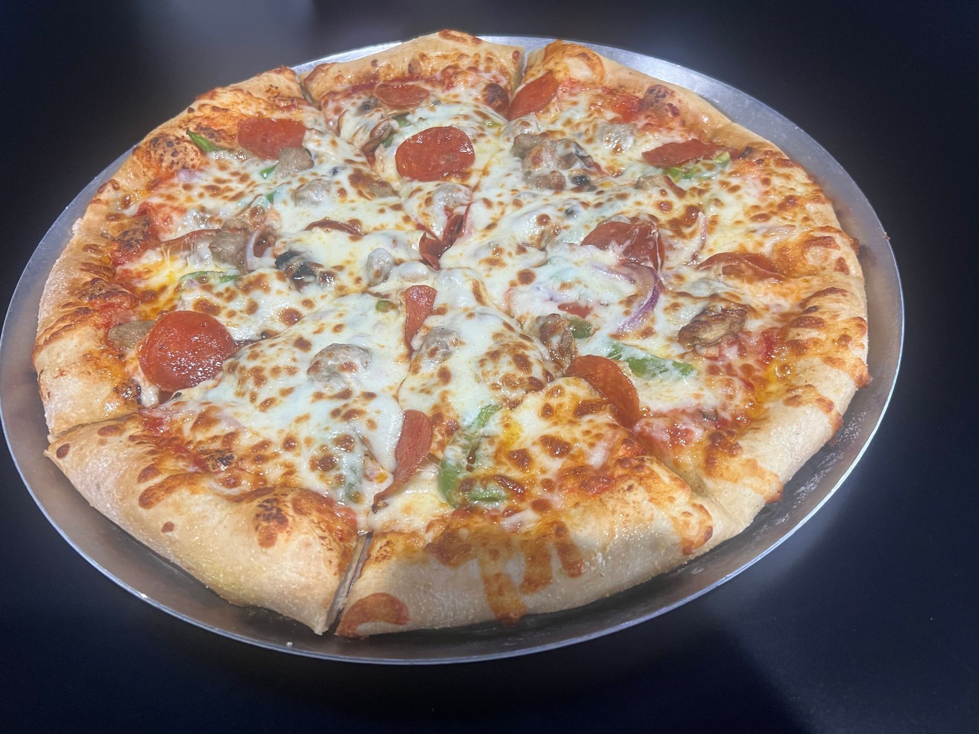 Pepperoni pizza with melted cheese on a dark plate, viewed from above.