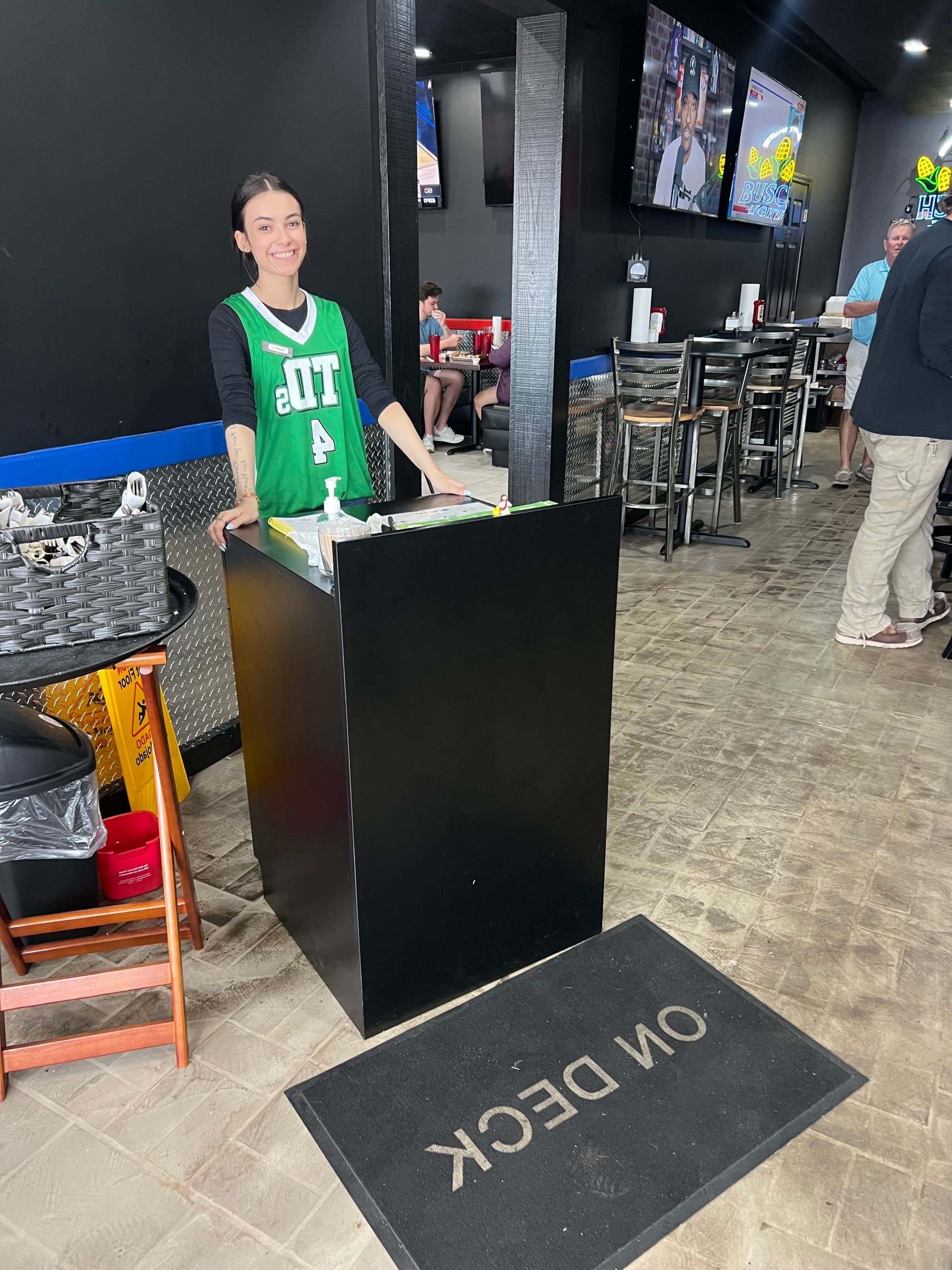 Person standing at a podium inside a restaurant, wearing a green Celtics jersey; 