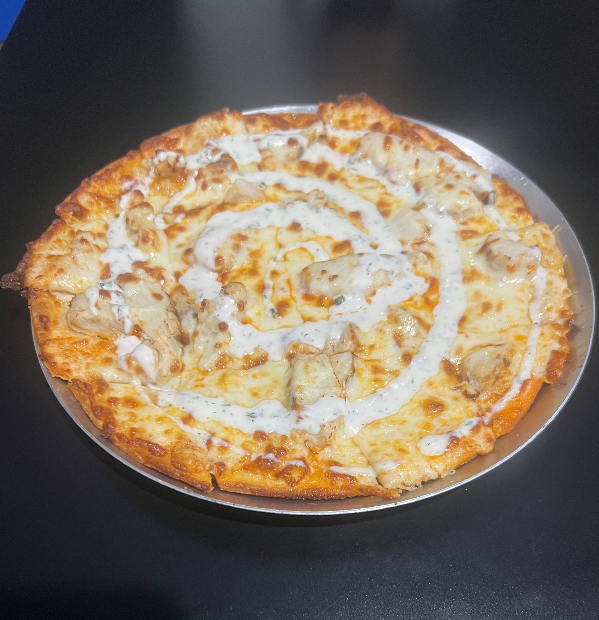 Cheese pizza with white drizzle on a round metal tray against a dark background