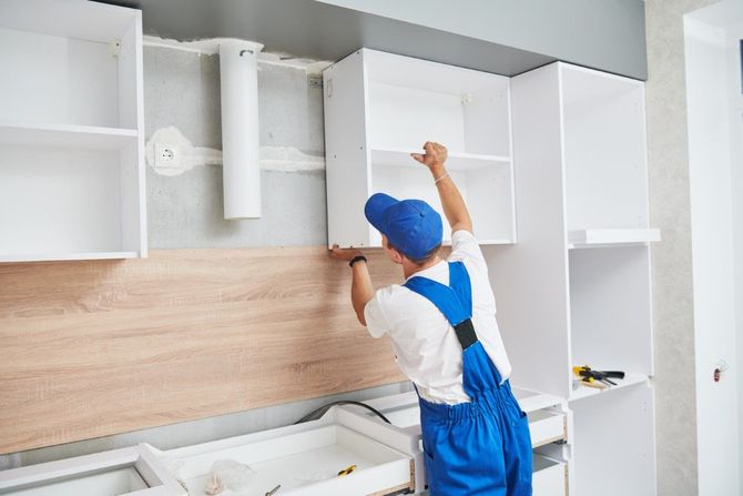 Worker installing white kitchen cabinets and wooden backsplash.