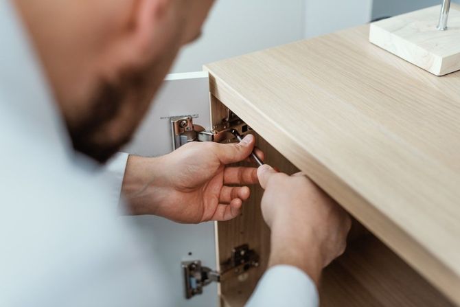 Person installing a cabinet hinge under a light wood countertop