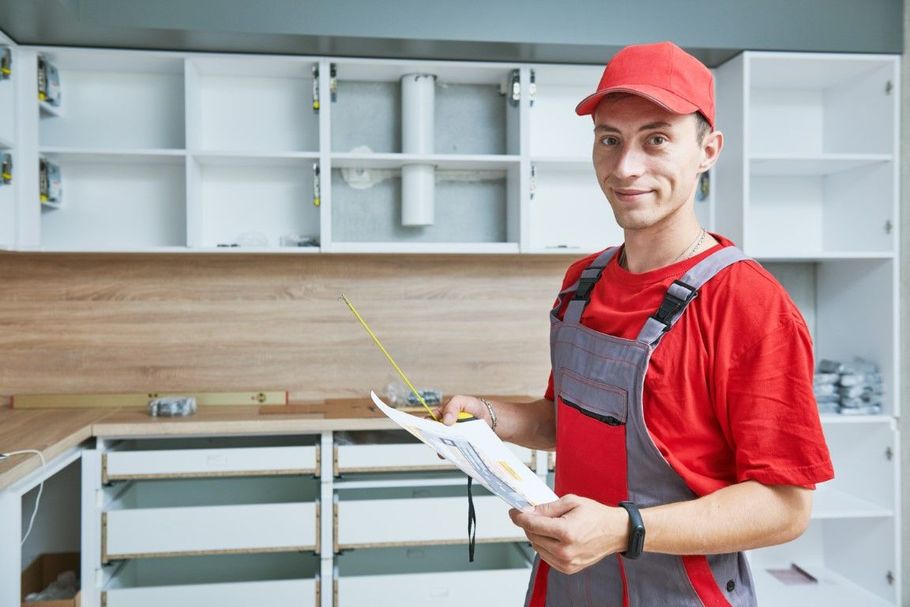 Worker in red cap and overalls holding a clipboard in a bright kitchen renovation space
