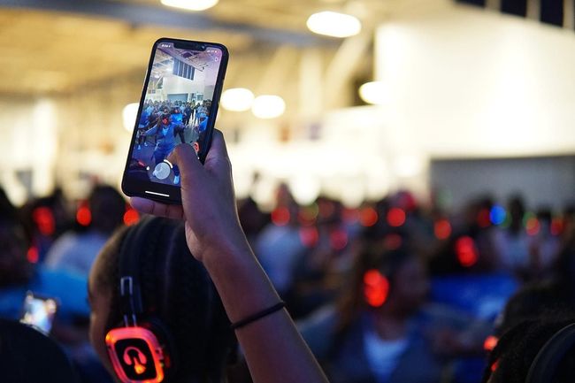 A person wearing headphones is taking a picture of a crowd with a cell phone.