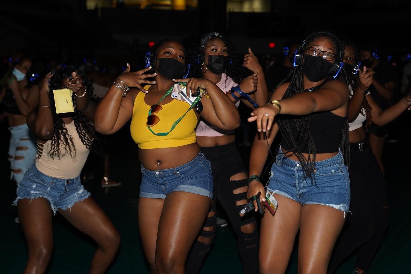 A group of women wearing masks and headphones are dancing at a party.
