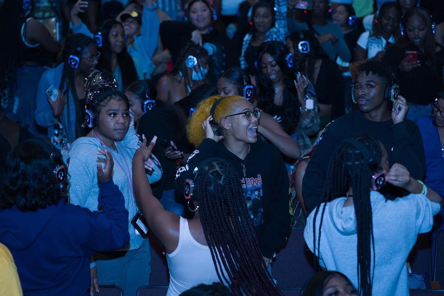 A crowd of people wearing headphones are dancing in a dark room.