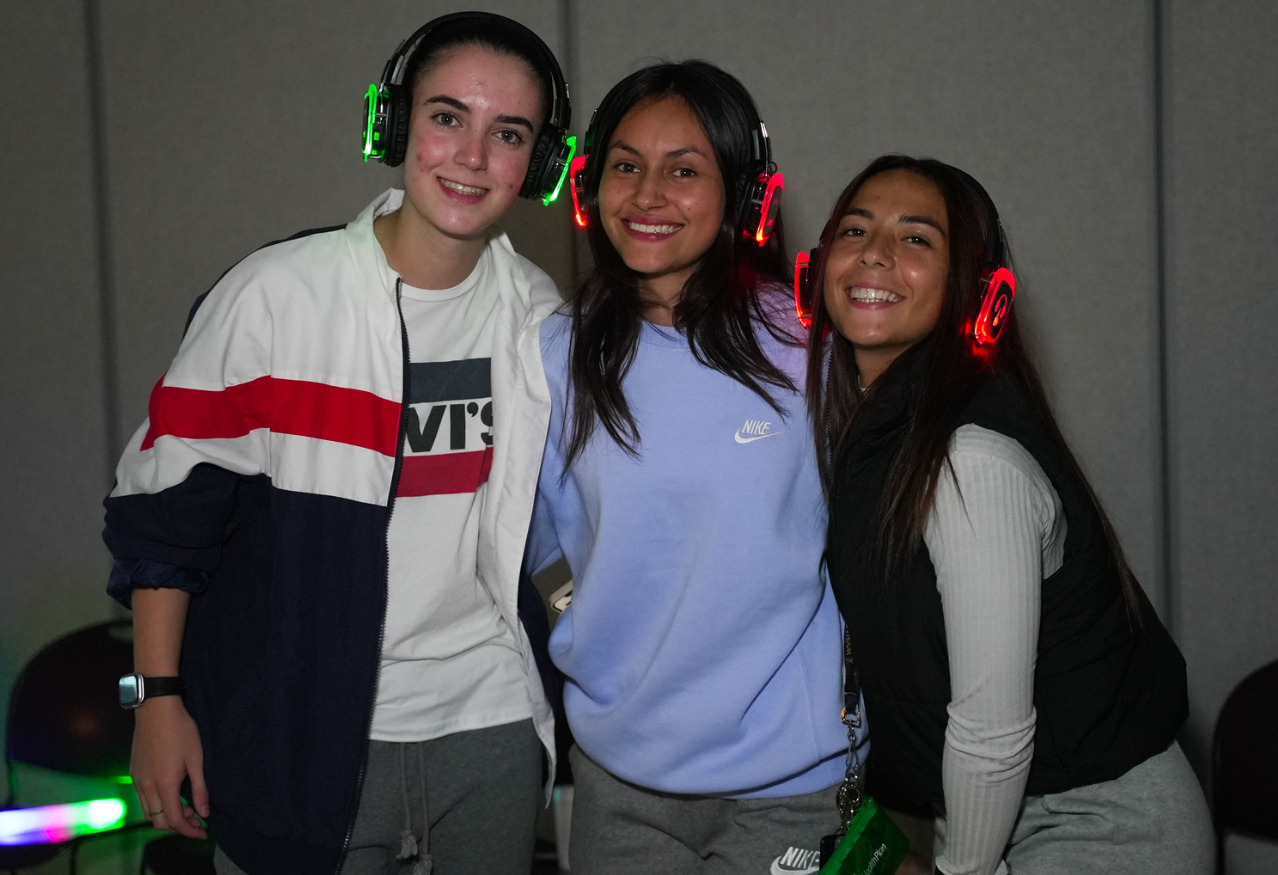 A crowd of people wearing headphones are dancing in a dark room.