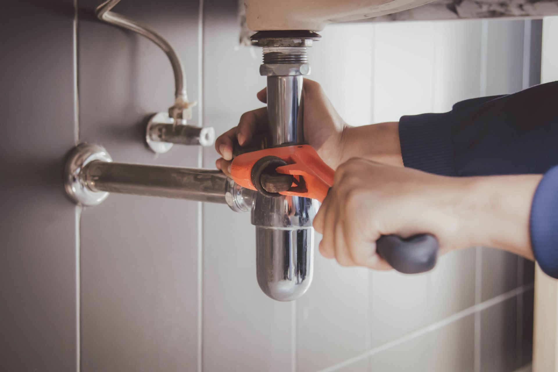A plumber is fixing a sink pipe with a wrench.