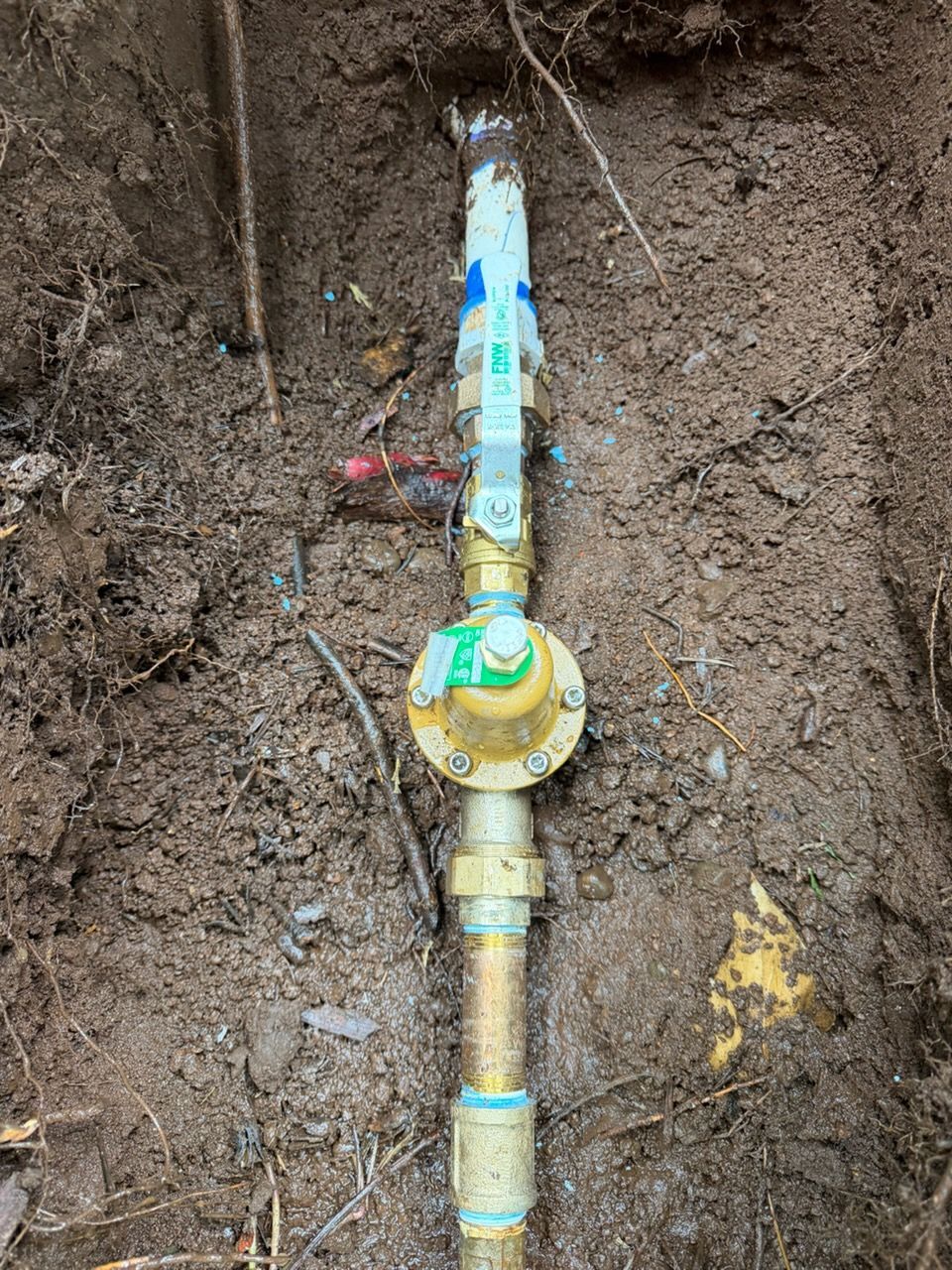 Exposed underground water valve assembly in a dirt trench, with yellow and blue pipe fittings.