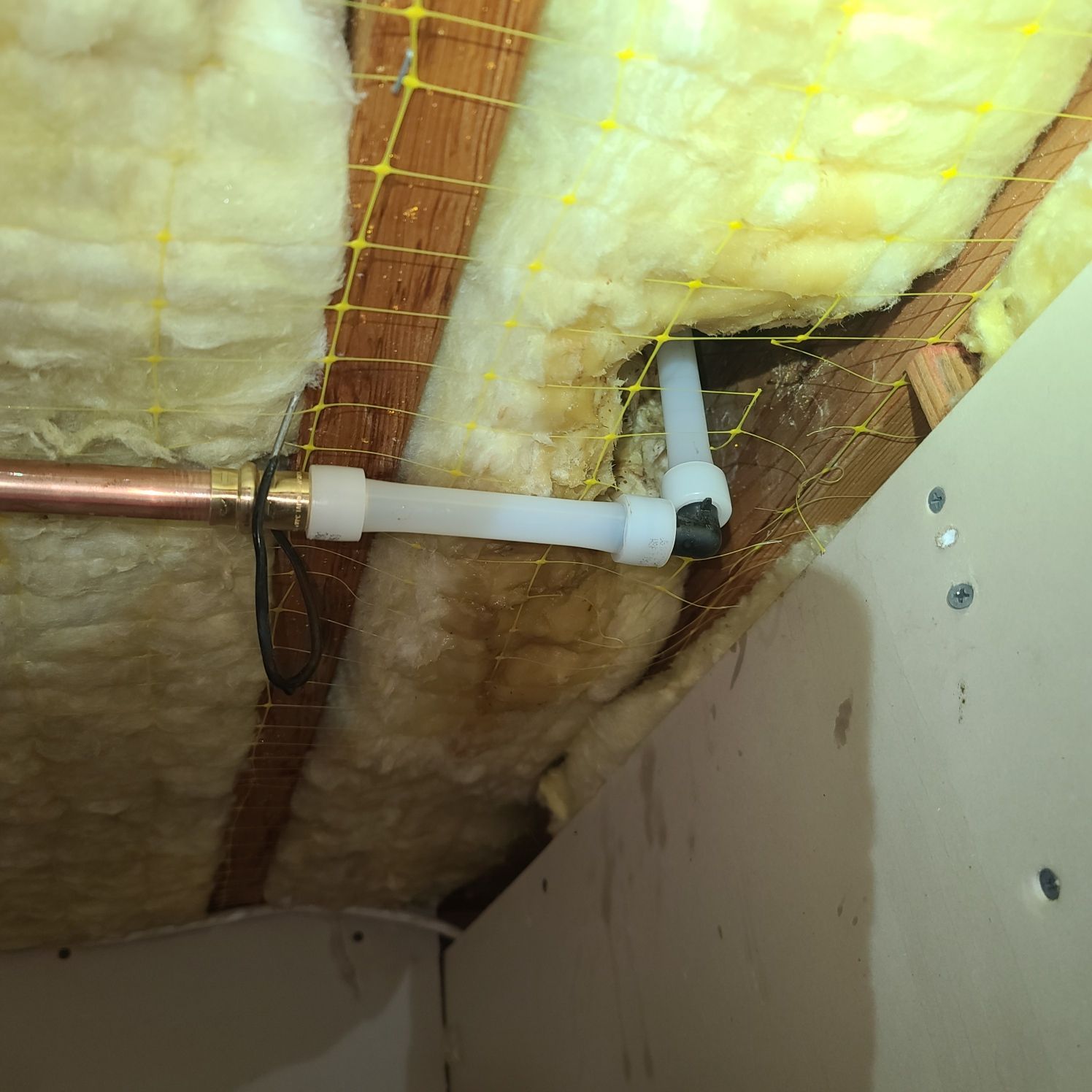 Pipes in an attic space. Copper and white plastic water pipes connected, surrounded by insulation and netting.