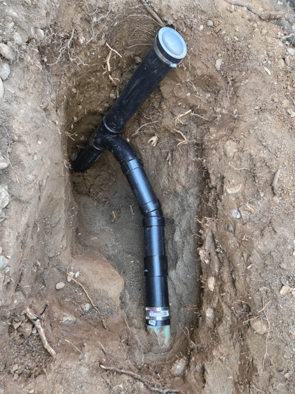 Black plastic drainage pipe in a dirt trench.