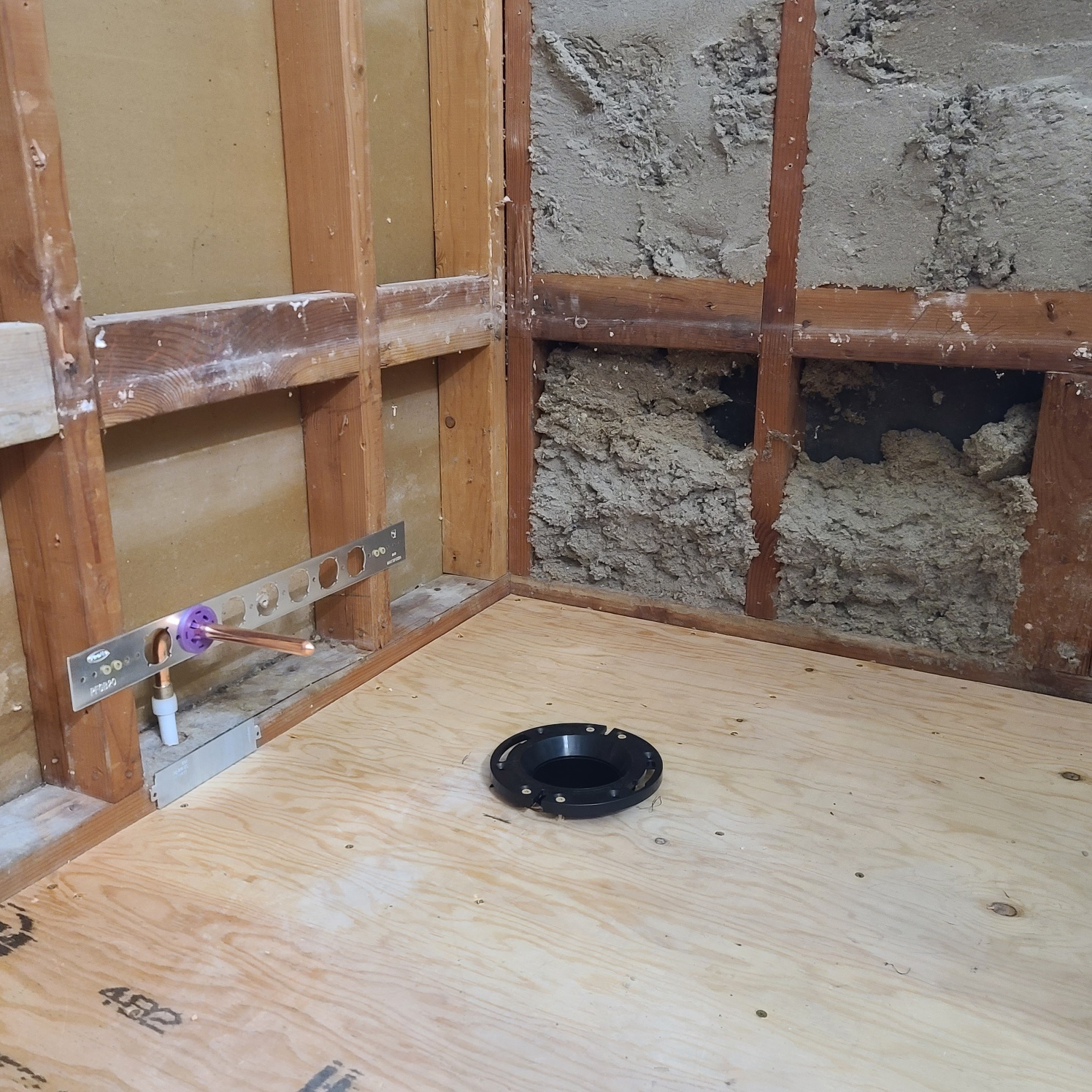 Shower stall construction in progress; wooden frame, plywood floor, plumbing, and exposed insulation.