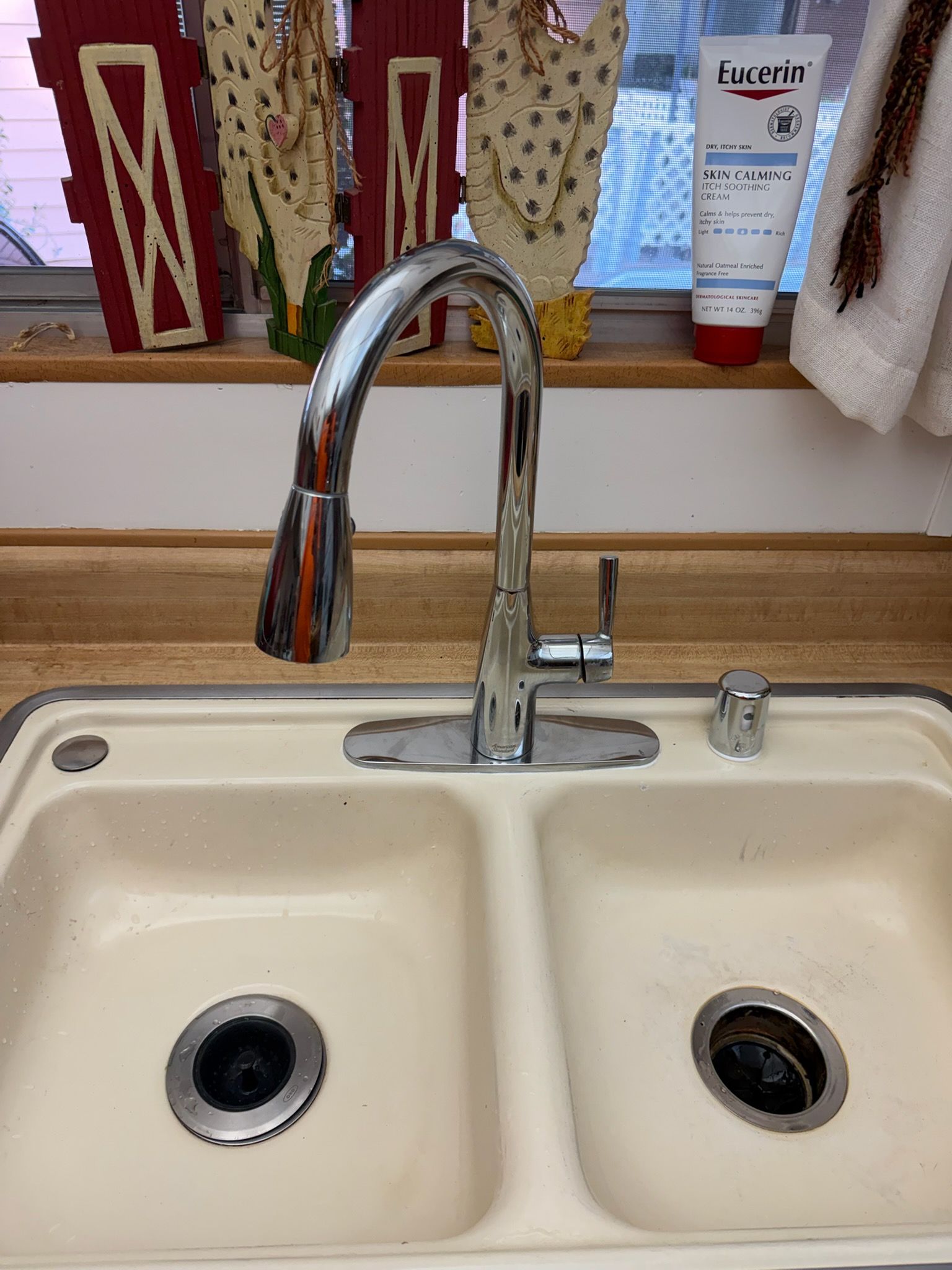 A chrome, high-arc kitchen faucet with a pull-down sprayer sits centered on a beige double-basin sink.