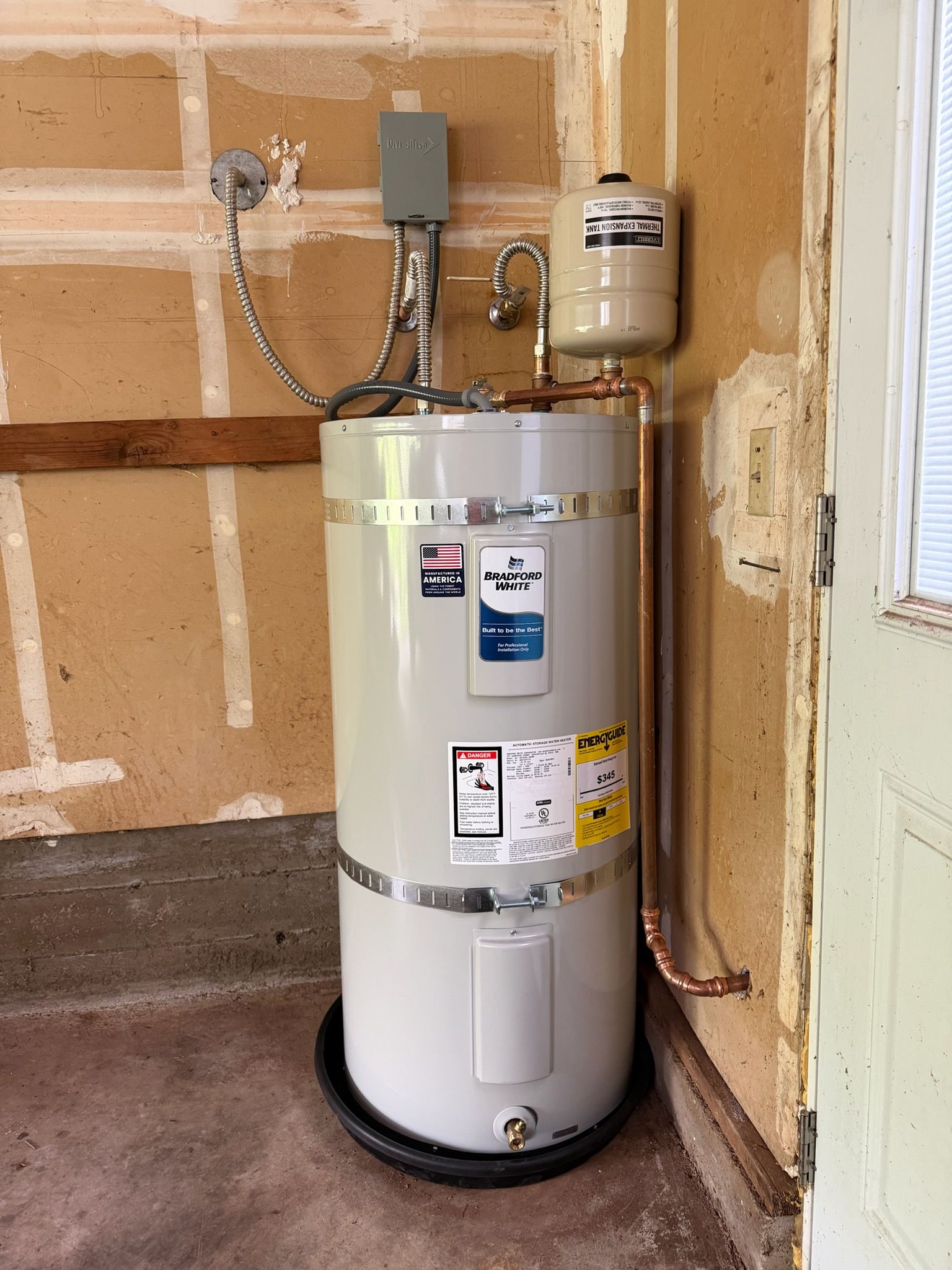 White water heater in a garage corner with exposed pipes, valves, and drywall.