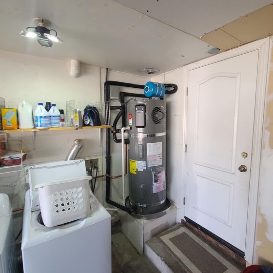 A wall-mounted, white tankless water heater installed in a basement.