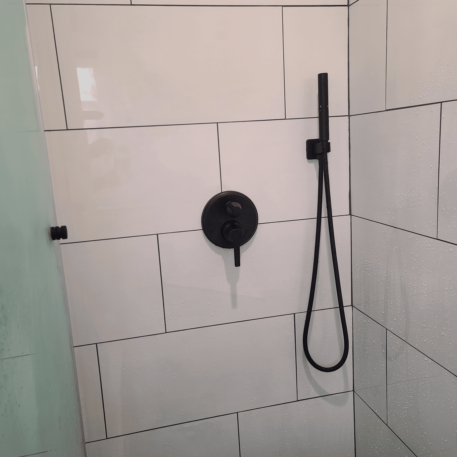 Black shower fixtures on white tiled wall. Shower head and controls are visible.