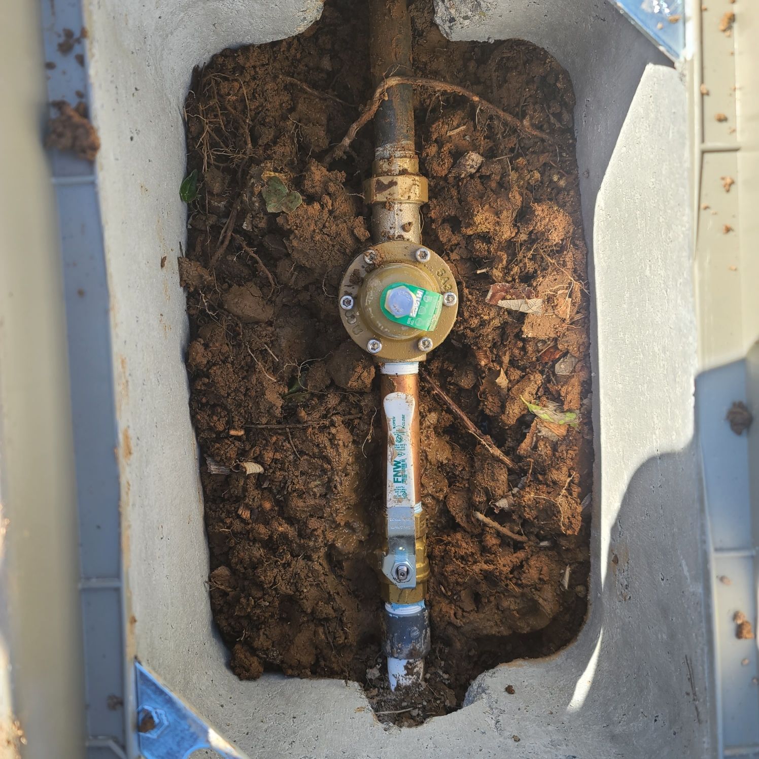 A brass water pressure regulator installed in a concrete box underground, surrounded by dirt.