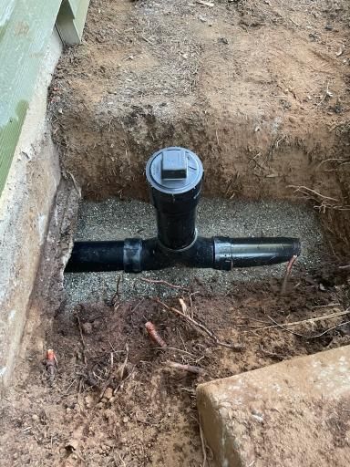 Black PVC pipe in a dirt excavation with a capped vertical section and horizontal T-connection.