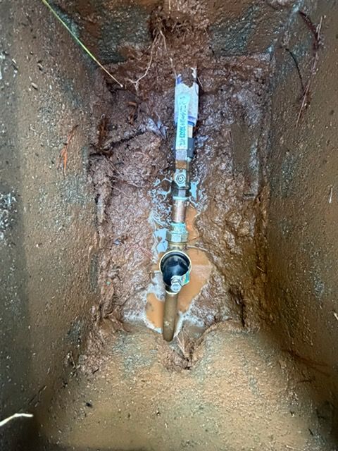 A water meter inside a muddy, rectangular underground utility box with a copper pipe and a shut-off valve.