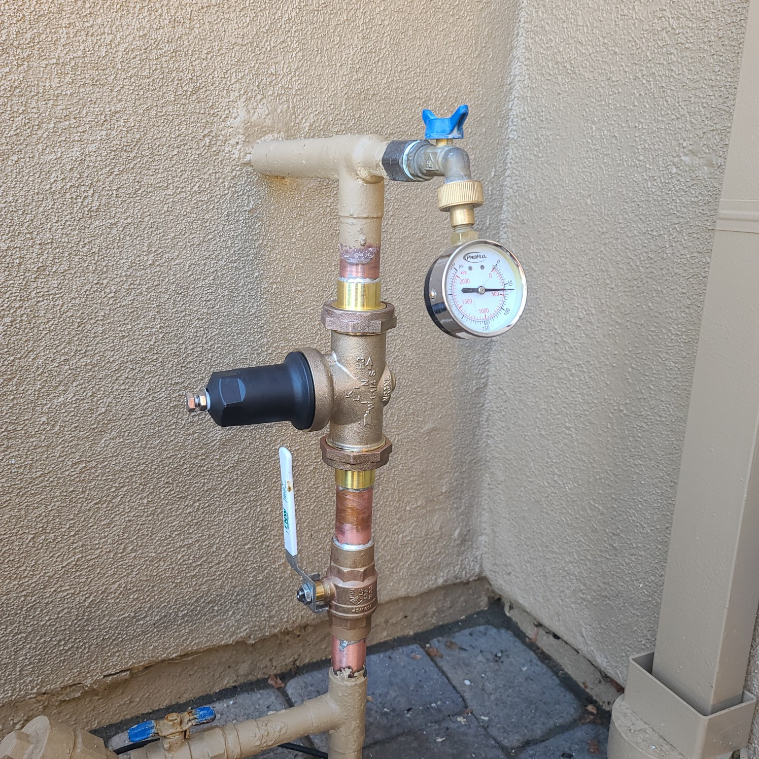 Plumbing system with pressure gauge and valve against a textured wall.